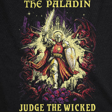 A close-up of a black graphic t-shirt featuring a fantasy illustration of a knight in shining silver armor with a red cape, holding a sword and shield, surrounded by red demons and purple skulls. The text 'THE PALADIN' is printed at the top and 'JUDGE THE WICKED' at the bottom in yellow.